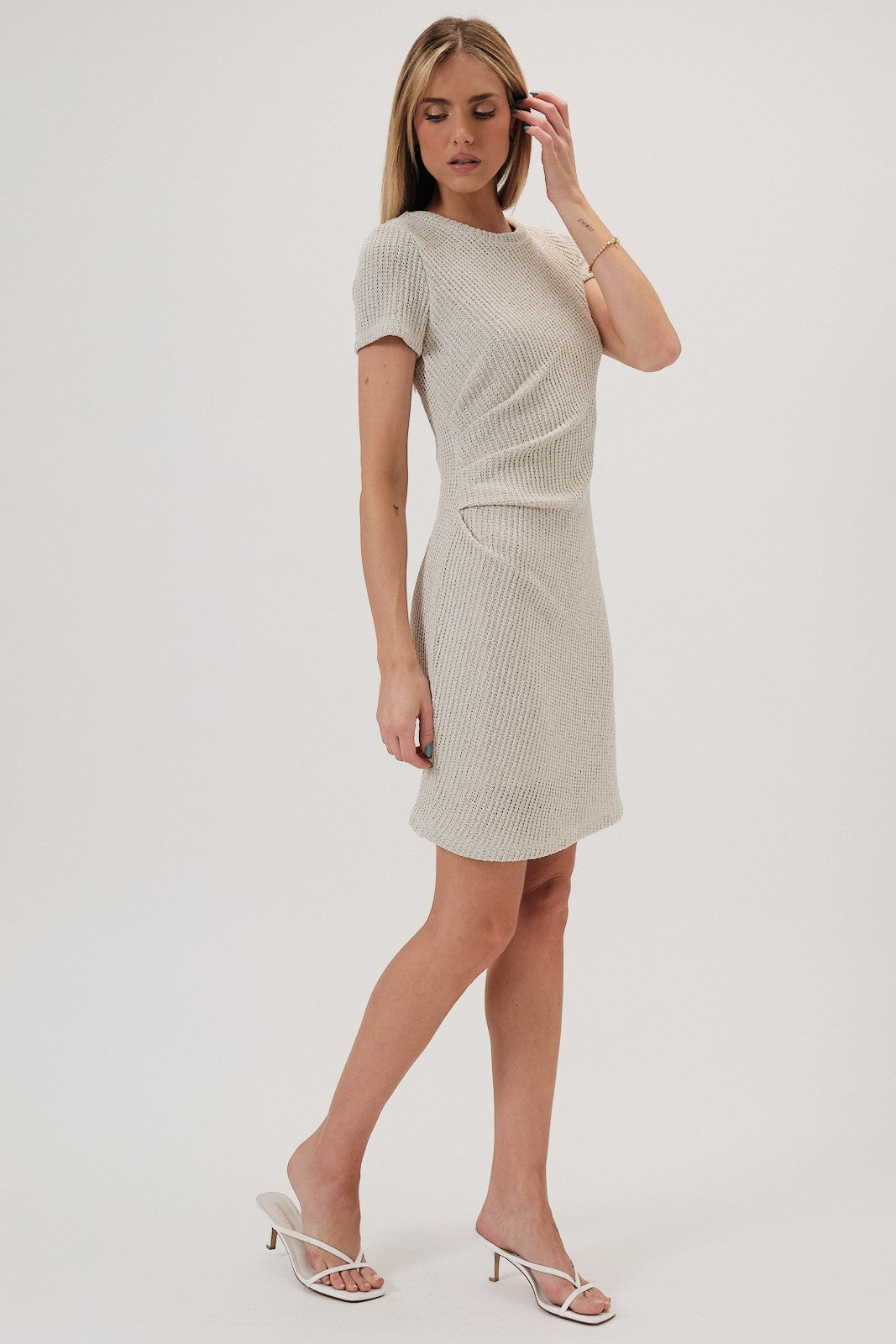 Woman wearing a beige boucle knit dress with side pleats on a white background