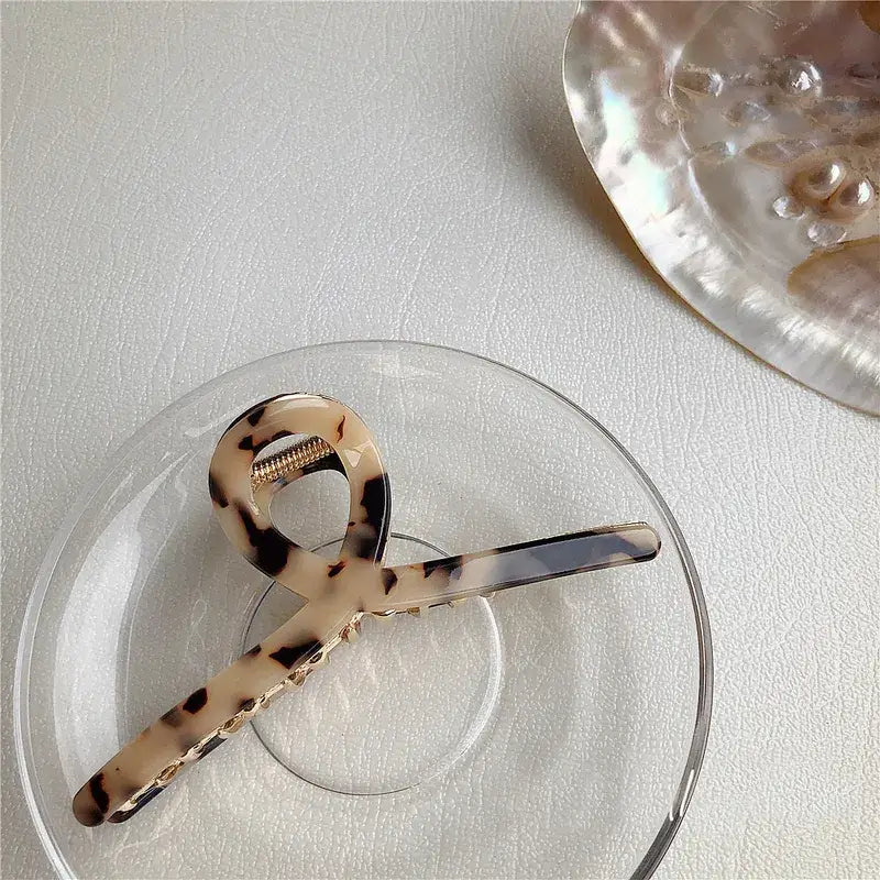 Tortoiseshell hair claw on a clear glass plate with a shell in the background