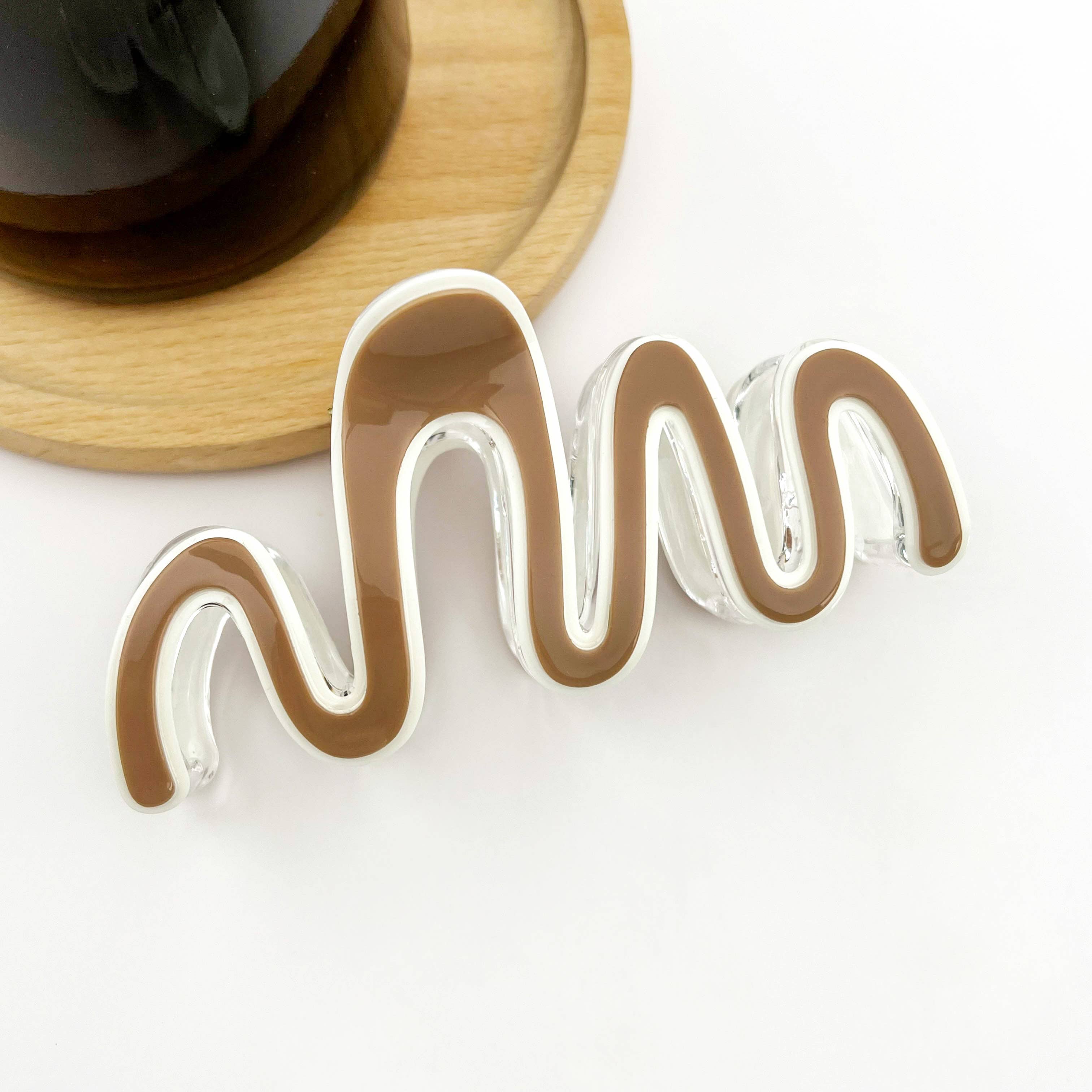 Large wave claw clip on a white surface with a wooden coaster in the background.