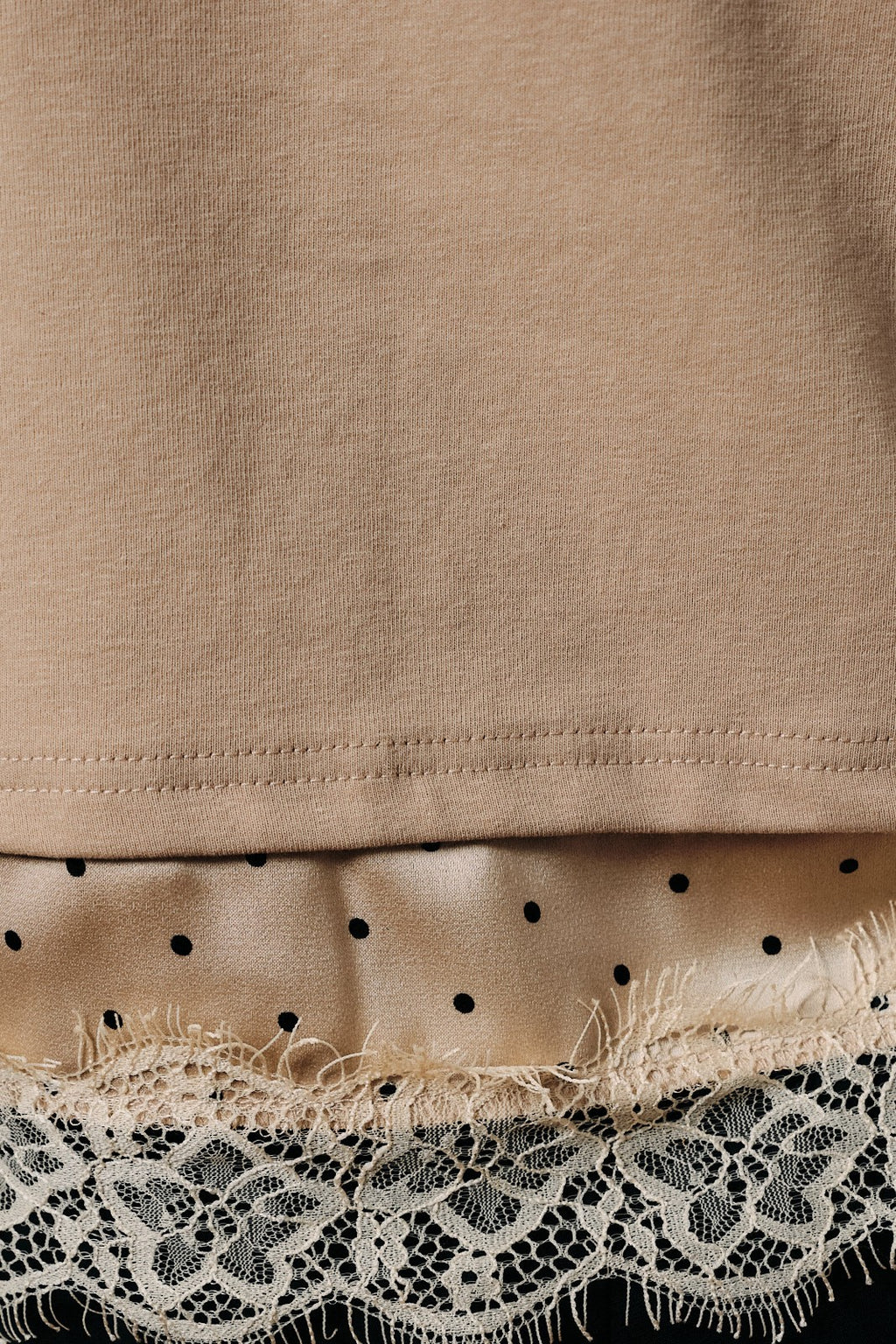 Close-up of a taupe knit garment with lace and satin trim at the bottom.