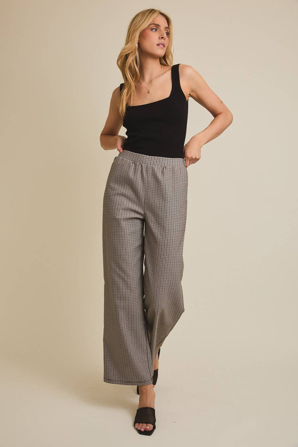 Woman wearing checkered pants a black tank top against a beige background