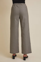 Woman wearing checkered pants showing back profile on a beige background