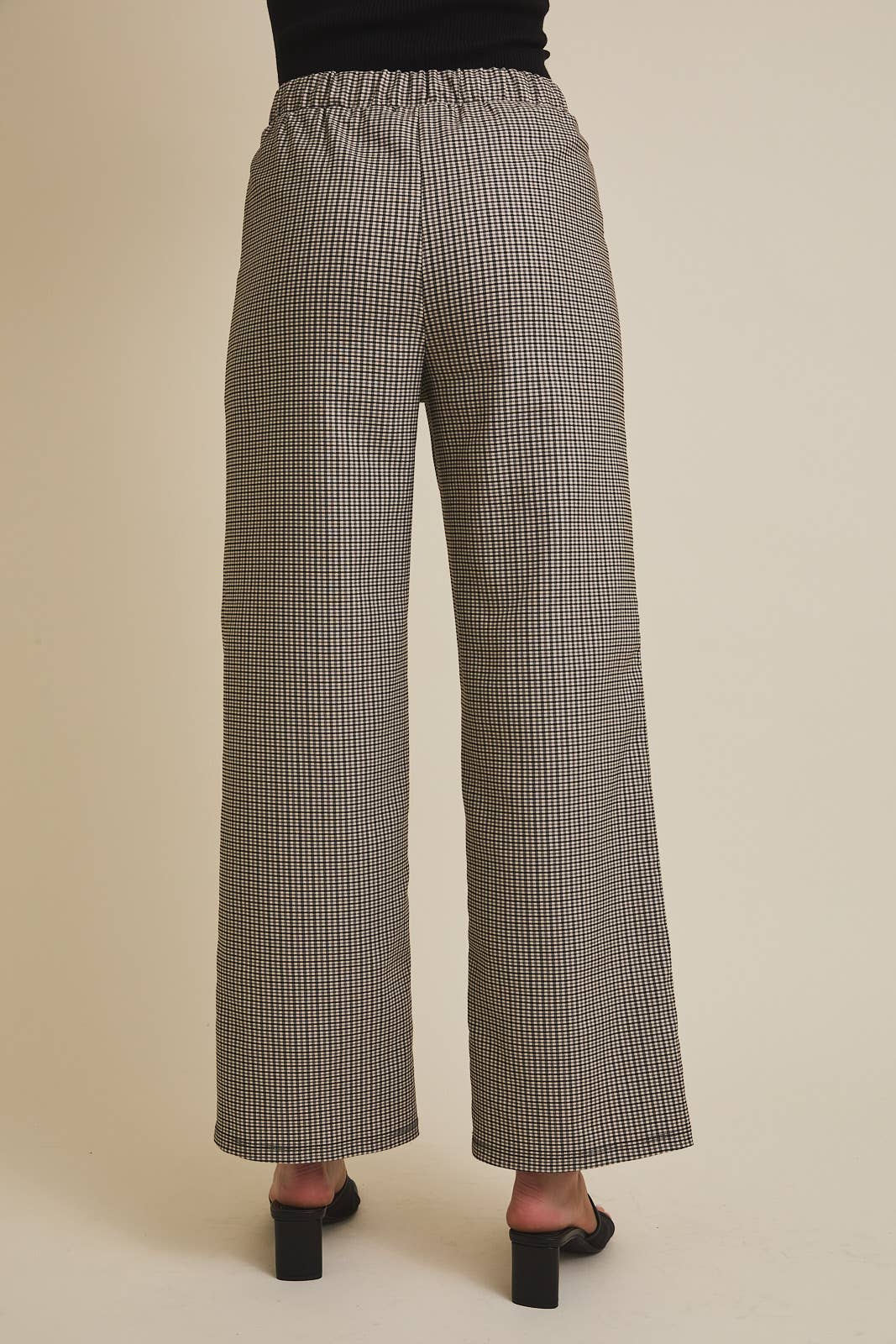 Woman wearing checkered pants showing back profile on a beige background