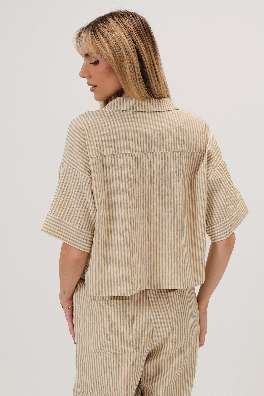 Back viewof a woman wearing a beige striped top on a white background