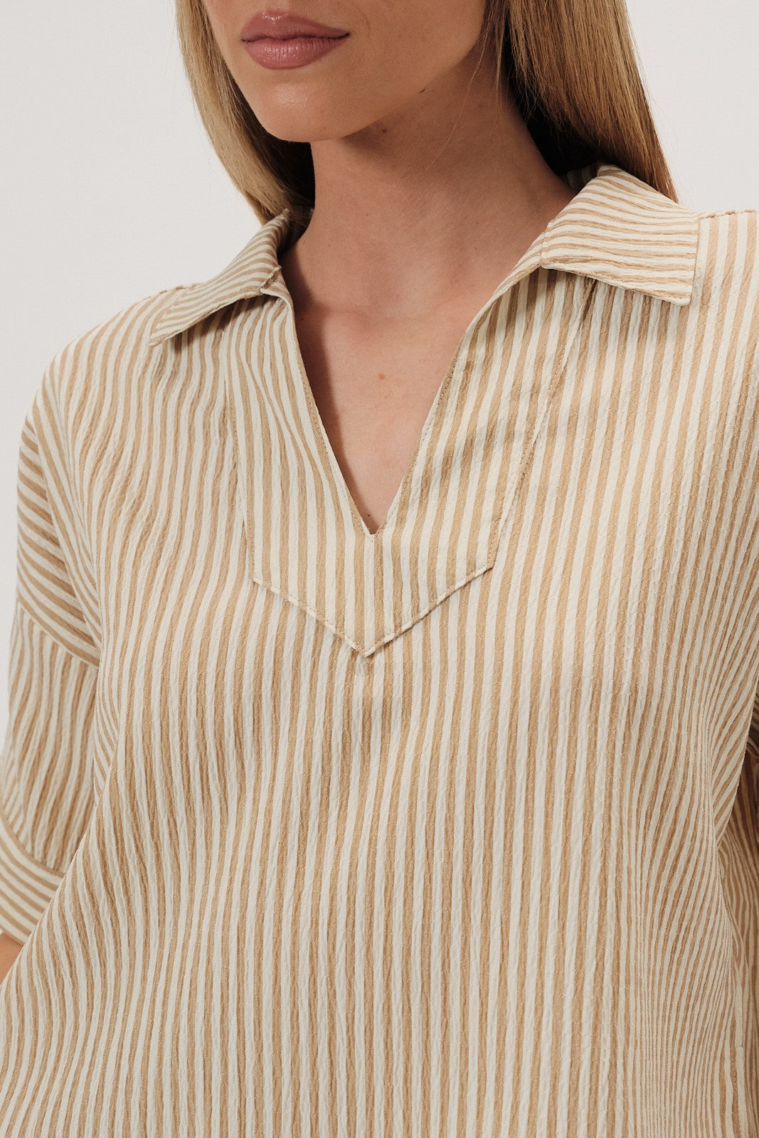 Woman wearing a beige striped top on a white background