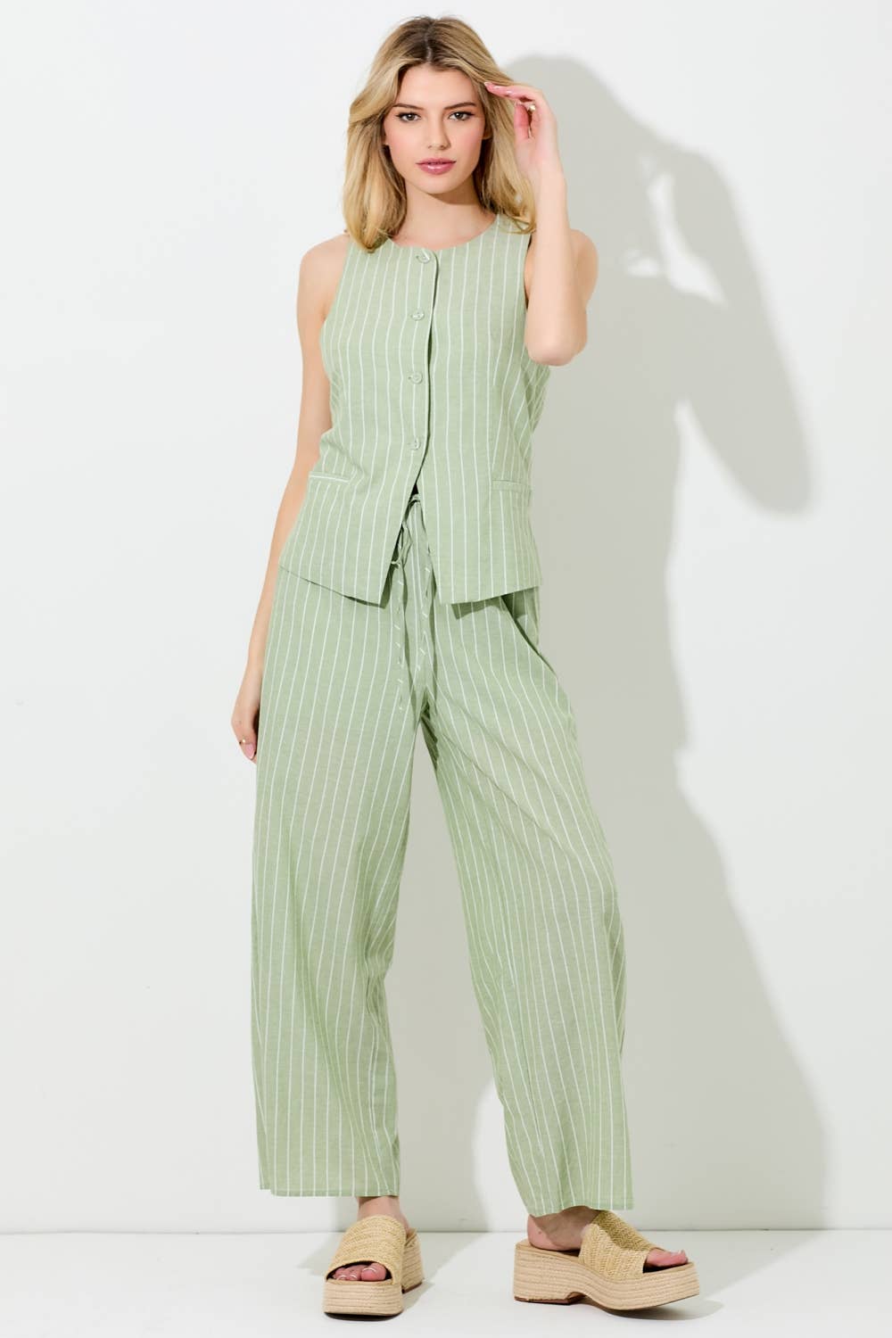 Woman wearing a matcha and ivory pinstripe button vest and pants on a grey background