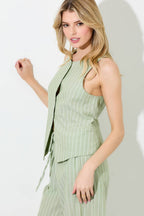 Woman wearing a matcha and ivory pinstripe button vest and pants on a grey background