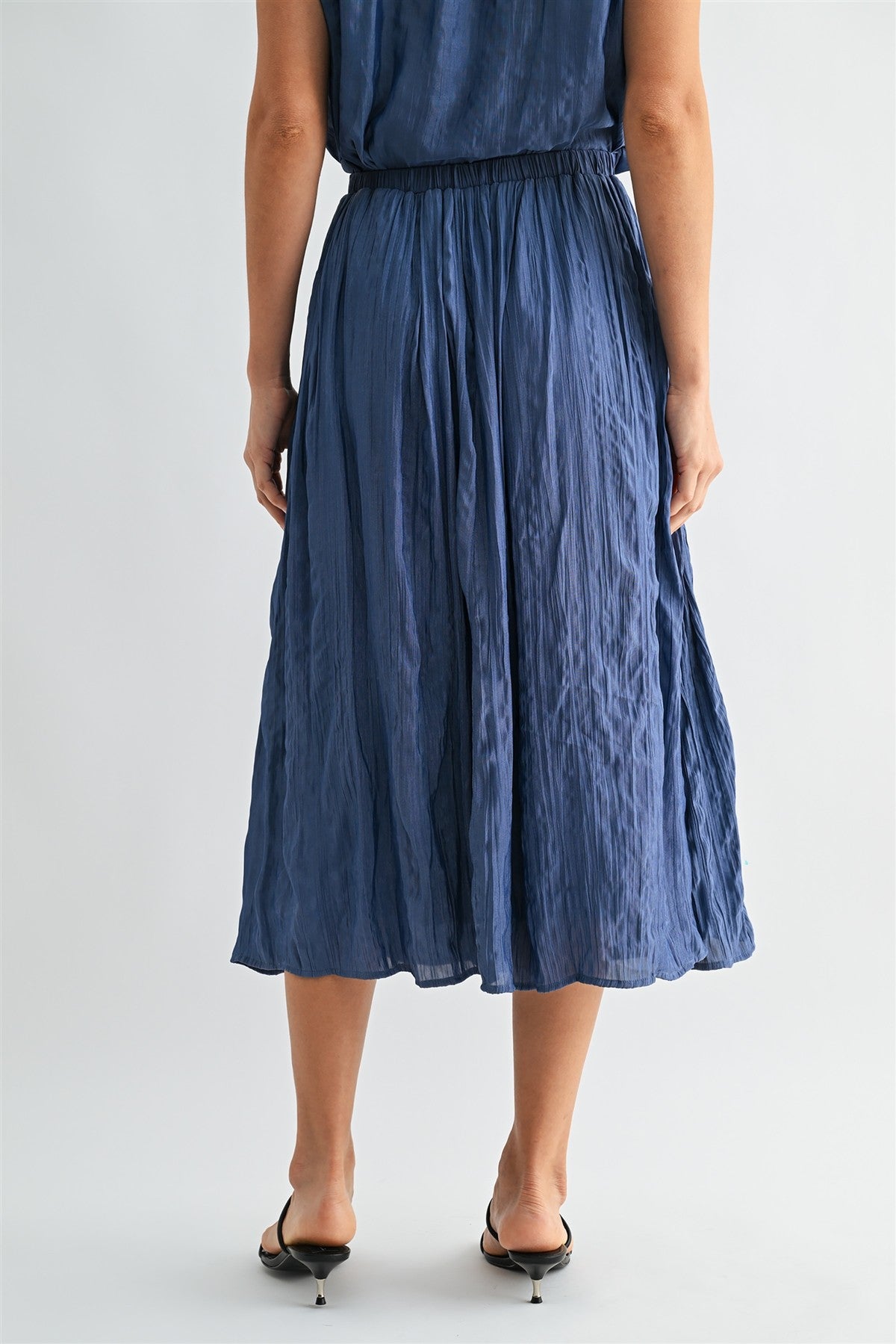 Back view of a woman wearing a dusty blue skirt on a white background