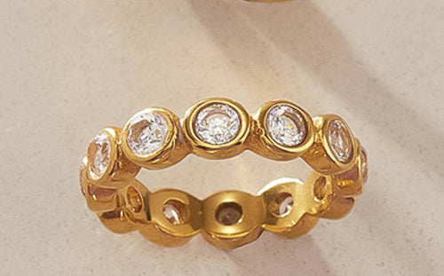A gold plated eternity-style ring with round cubic zirconia set in a repeating pattern, photographed on a grey background.