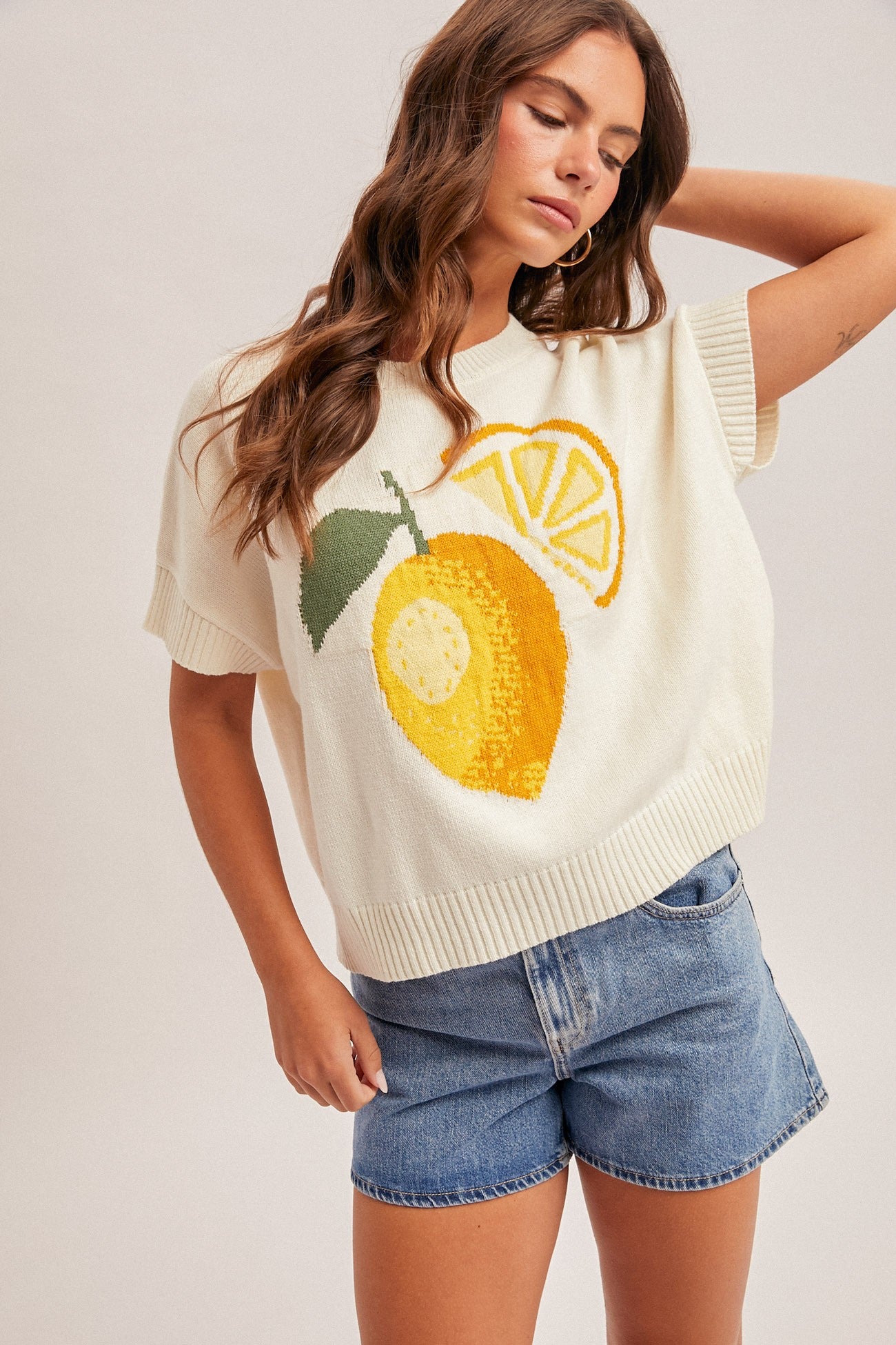 Woman wearing a cream sweater with lemon design on a plain background