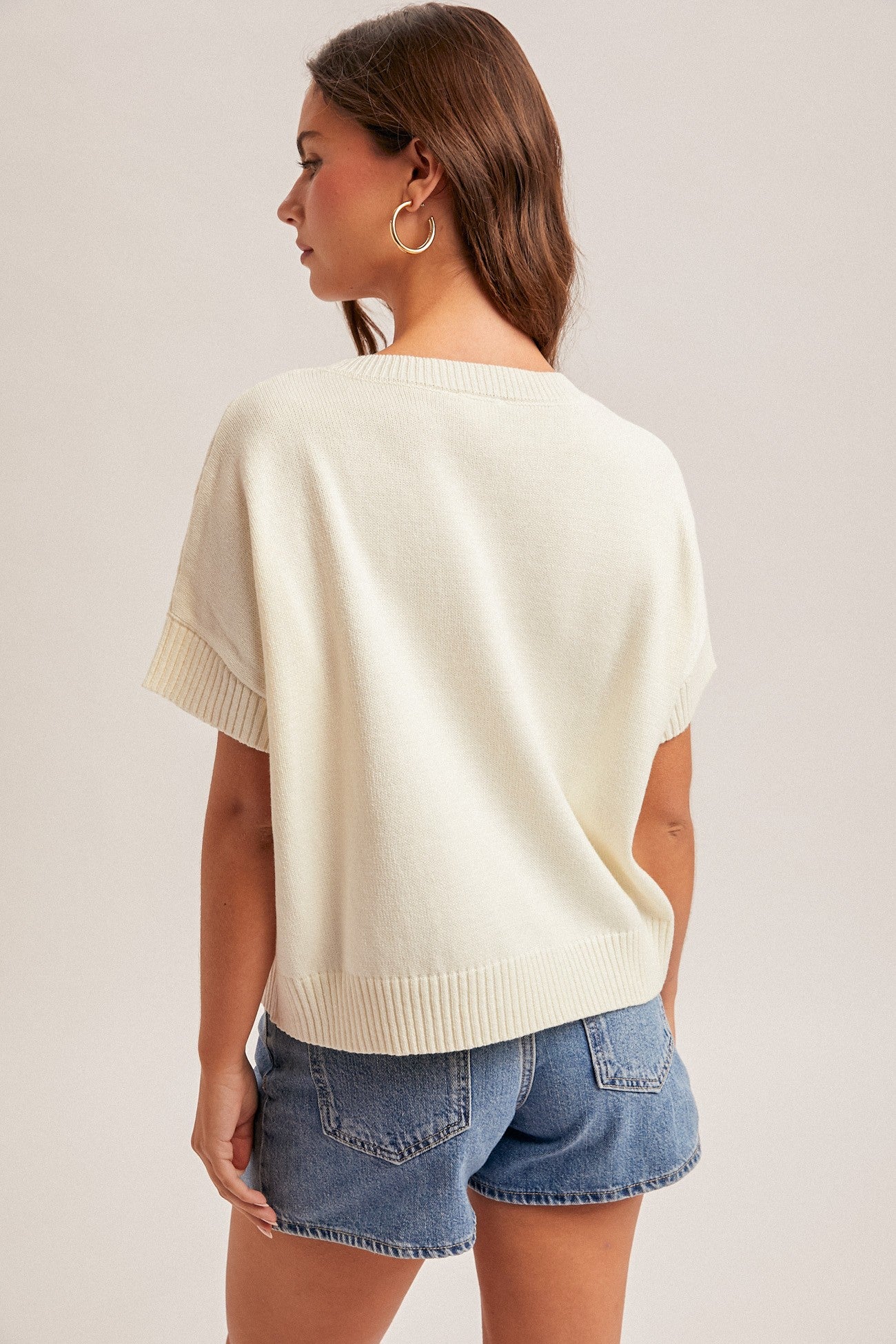 Back view of a woman wearing a cream sweater on a plain background