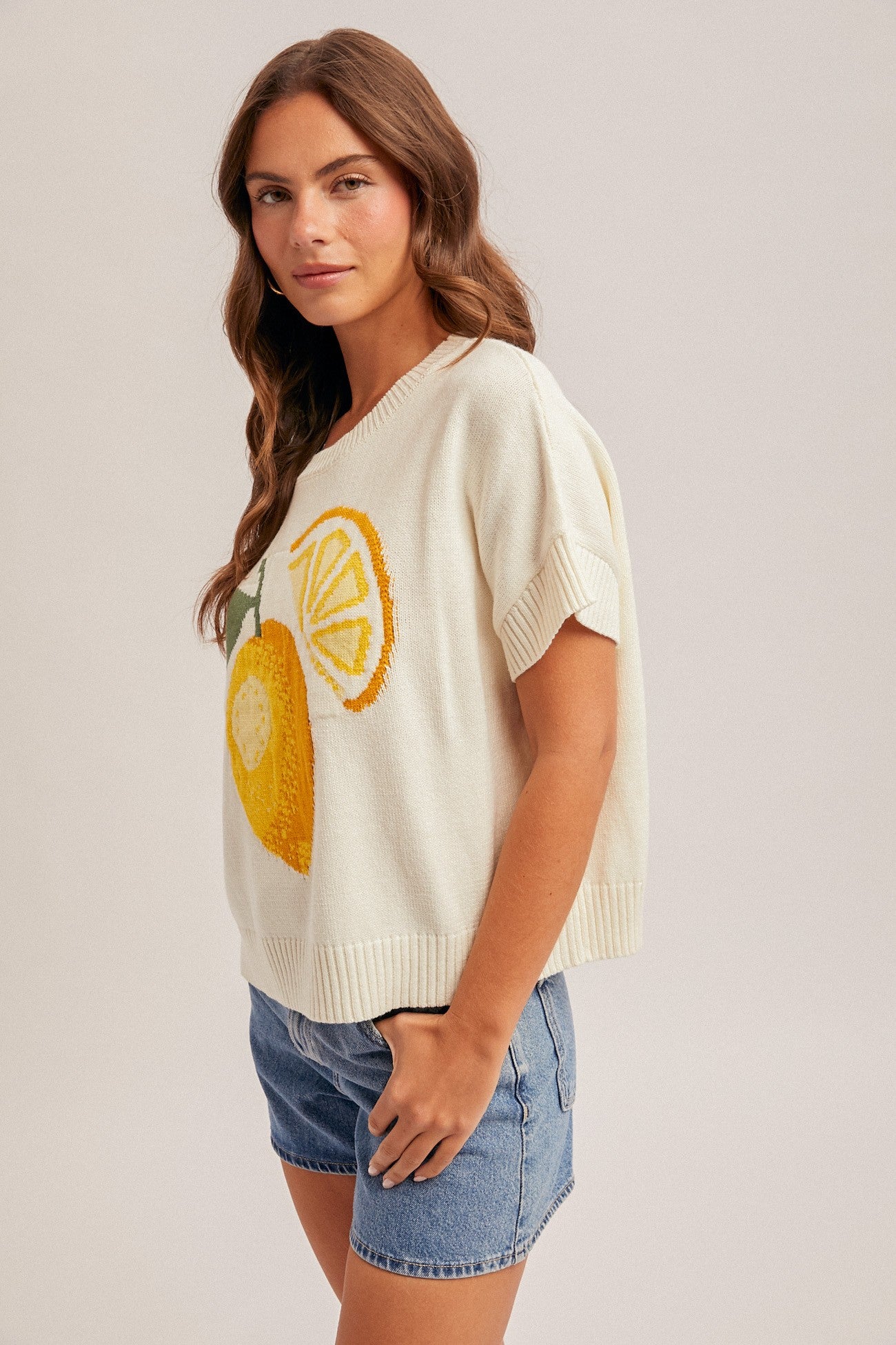 Woman wearing a cream sweater with lemon design on a plain background