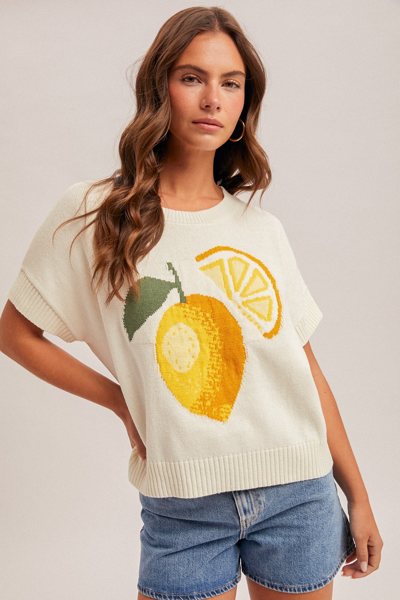 Woman wearing a cream sweater with lemon design on a plain background