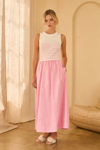 Woman wearing a maxi dress with pink and white striped top and a long pink skirt standing against beige walls 