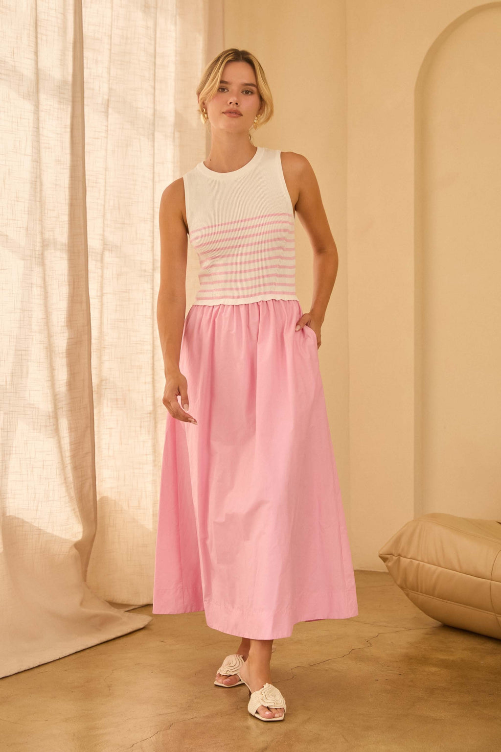 Woman wearing a maxi dress with pink and white striped top and a long pink skirt standing against beige walls