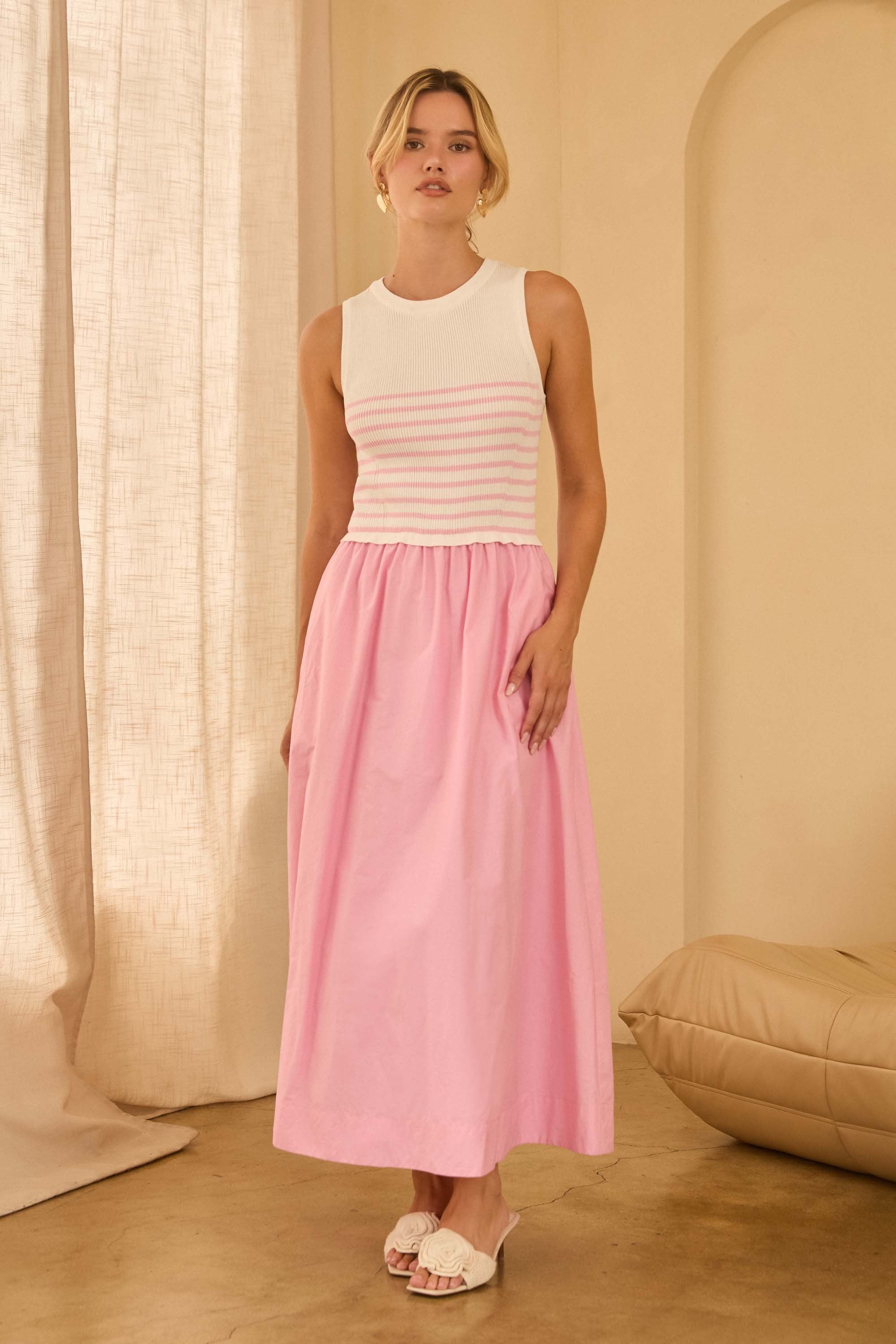 Woman wearing a maxi dress with pink and white striped top and a long pink skirt standing against beige walls