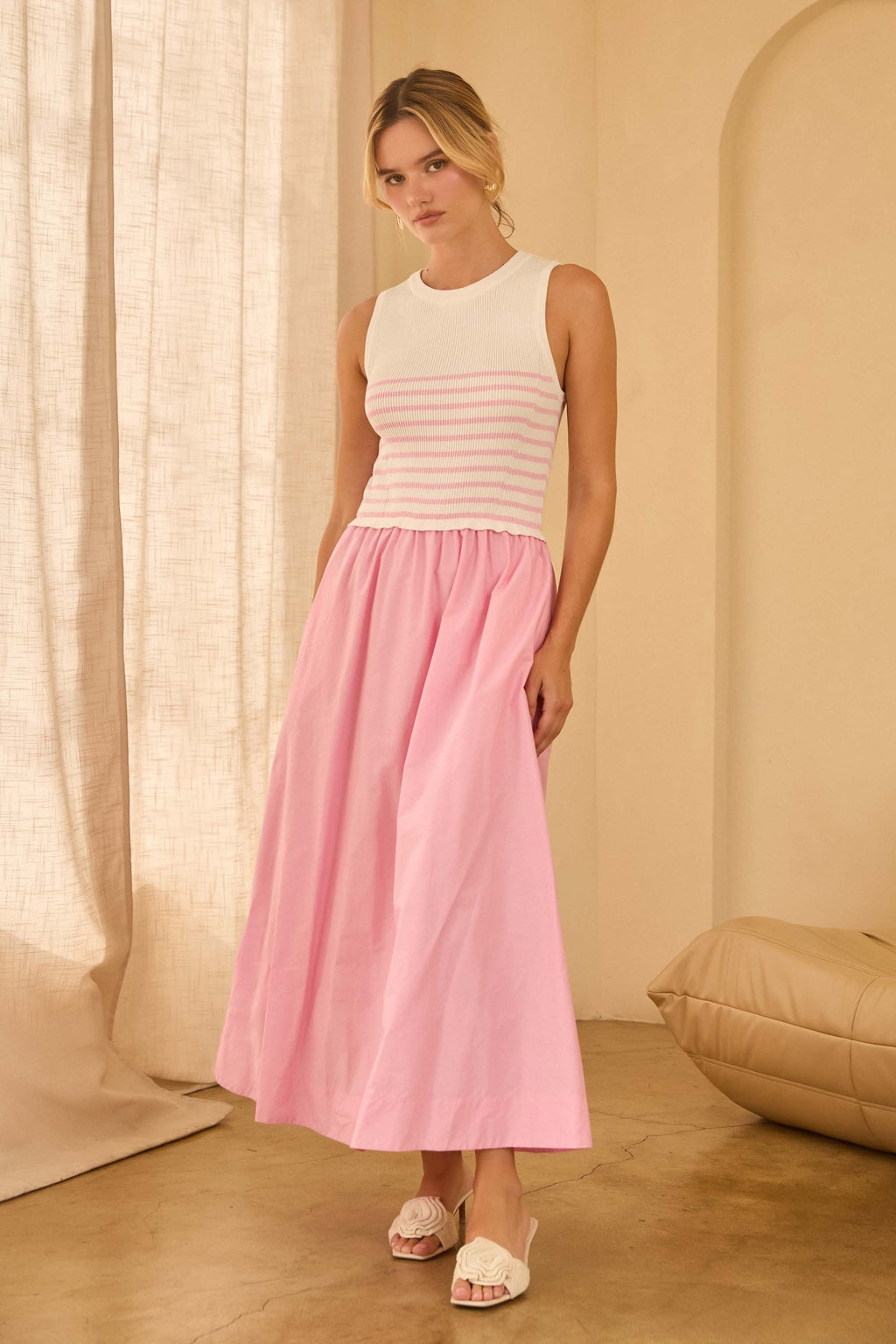 Woman wearing a maxi dress with pink and white striped top and a long pink skirt standing against beige walls