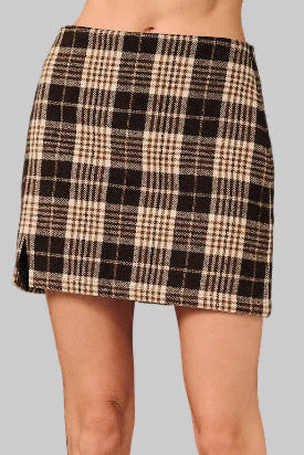 A woman wearing a brown and cream plaid mini skirt standing against a gray background 
