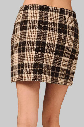 A back view of a woman wearing a brown and cream plaid mini skirt standing against a gray background 