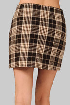 A back view of a woman wearing a brown and cream plaid mini skirt standing against a gray background 