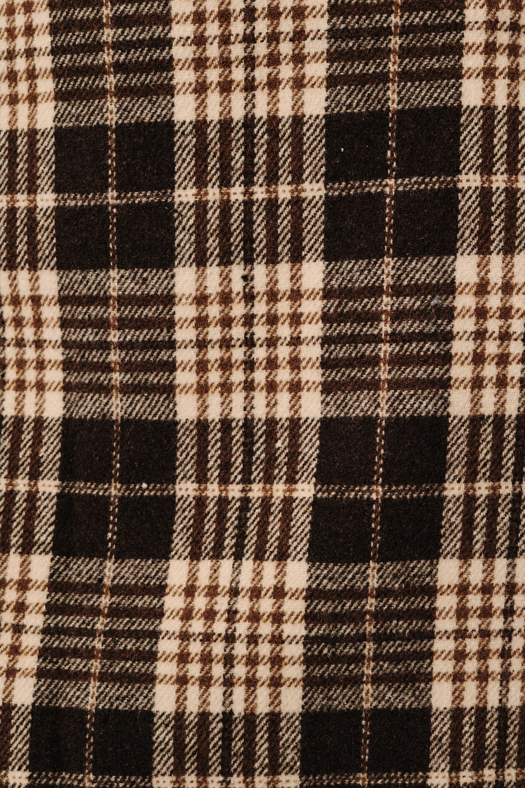 A close-up of a plaid fabric pattern with alternating blocks of black and warm cream, detailed with thin brown and beige intersecting lines.