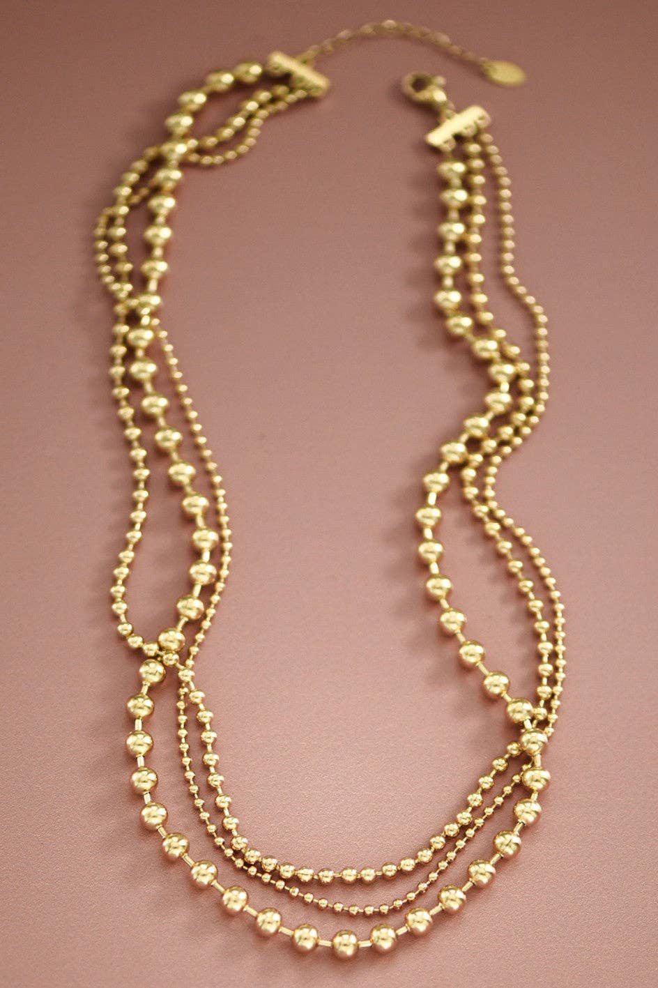 Gold triple chain beaded necklace on a pink background