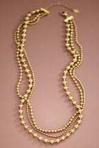 Gold triple chain beaded necklace on a pink background