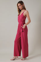 Woman wearing a fuchsia jumpsuit against a plain background