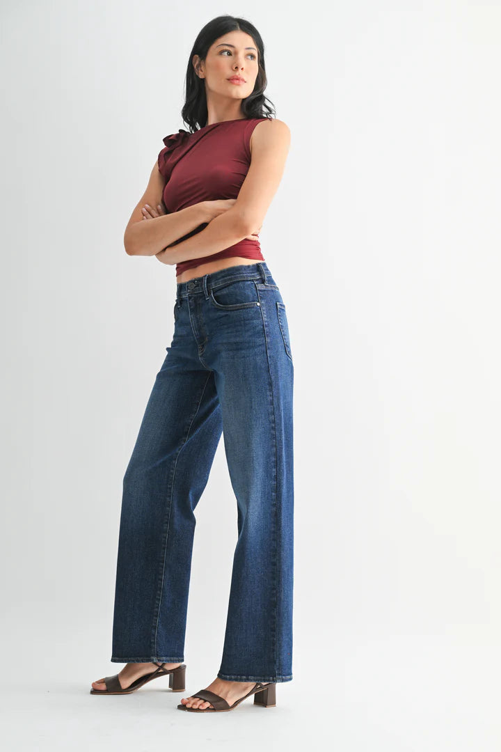 Woman wearing a burgundy top and dark wash jeans on a white background