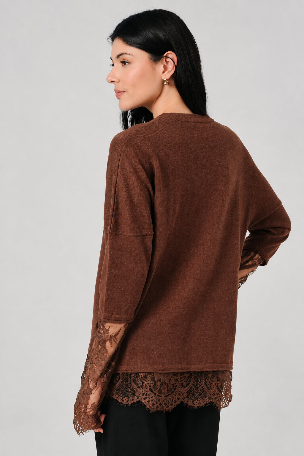 Back view of a woman wearing a small ribbed brown shirt with lace sleeves and hem against a white drape background