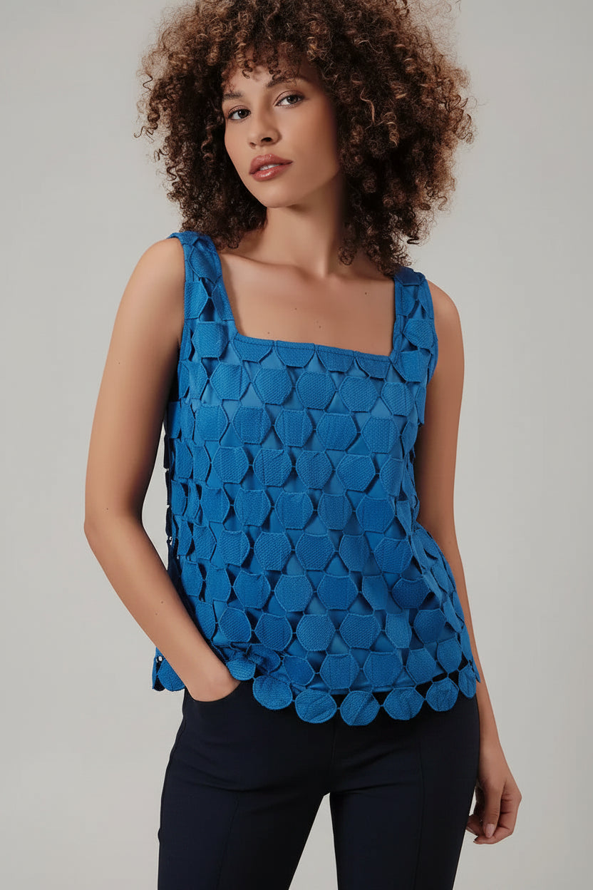 Woman wearing a blue sleeveless top with a lace applique overlay against a beige background
