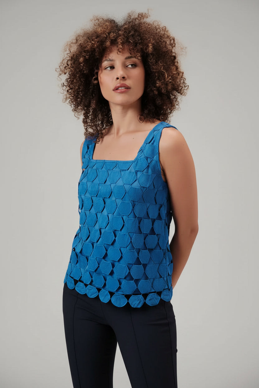 Woman wearing a blue sleeveless top with a lace applique overlay against a beige background