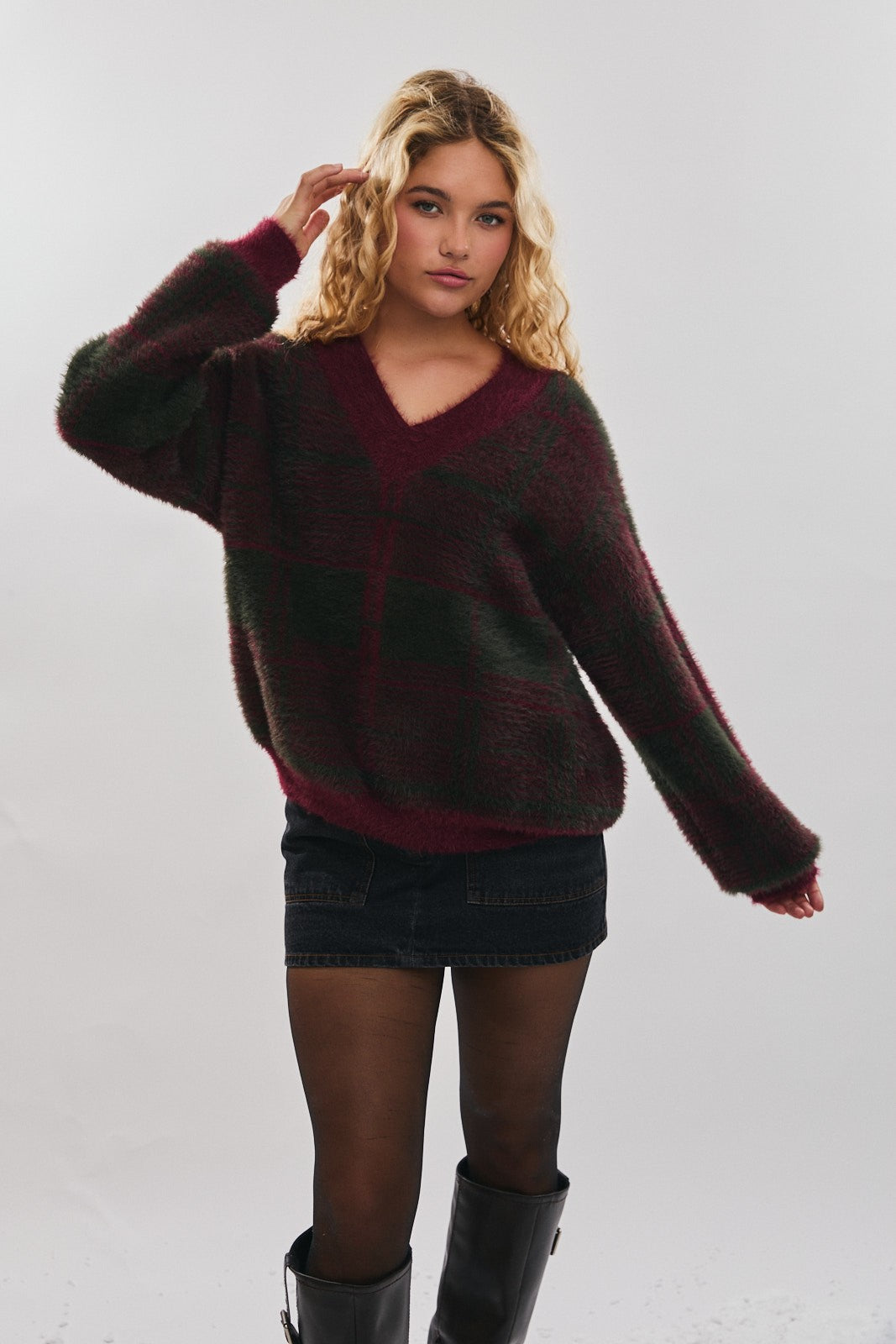 Woman wearing a muted burgundy and green plaid sweater and black skirt on a plain background
