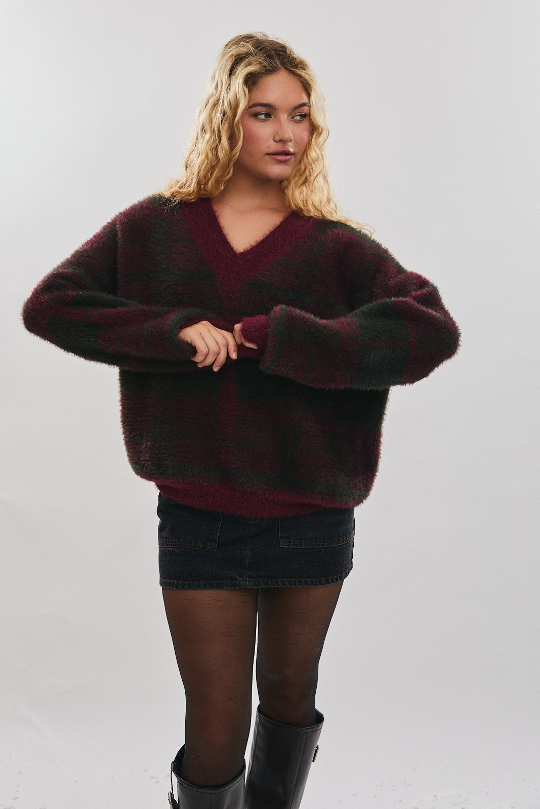 Woman wearing a muted burgundy and green plaid sweater with black skirt on a plain background
