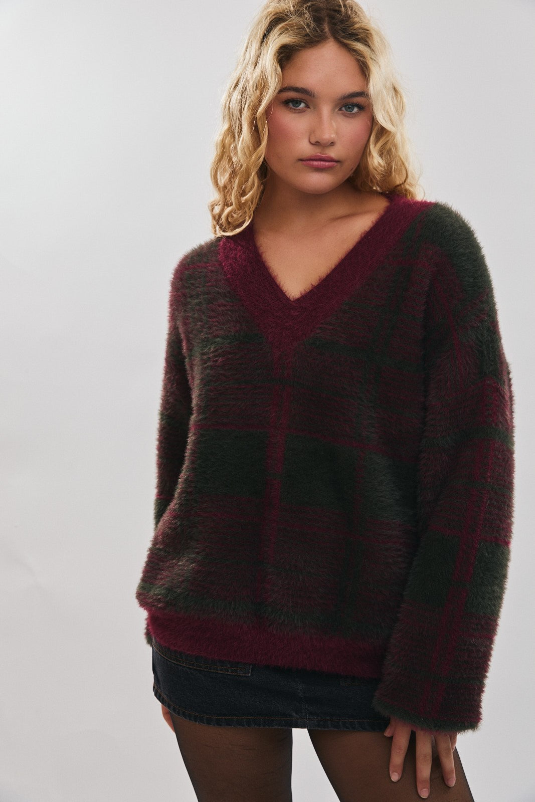 Woman wearing a muted burgundy and green plaid sweater on a plain background