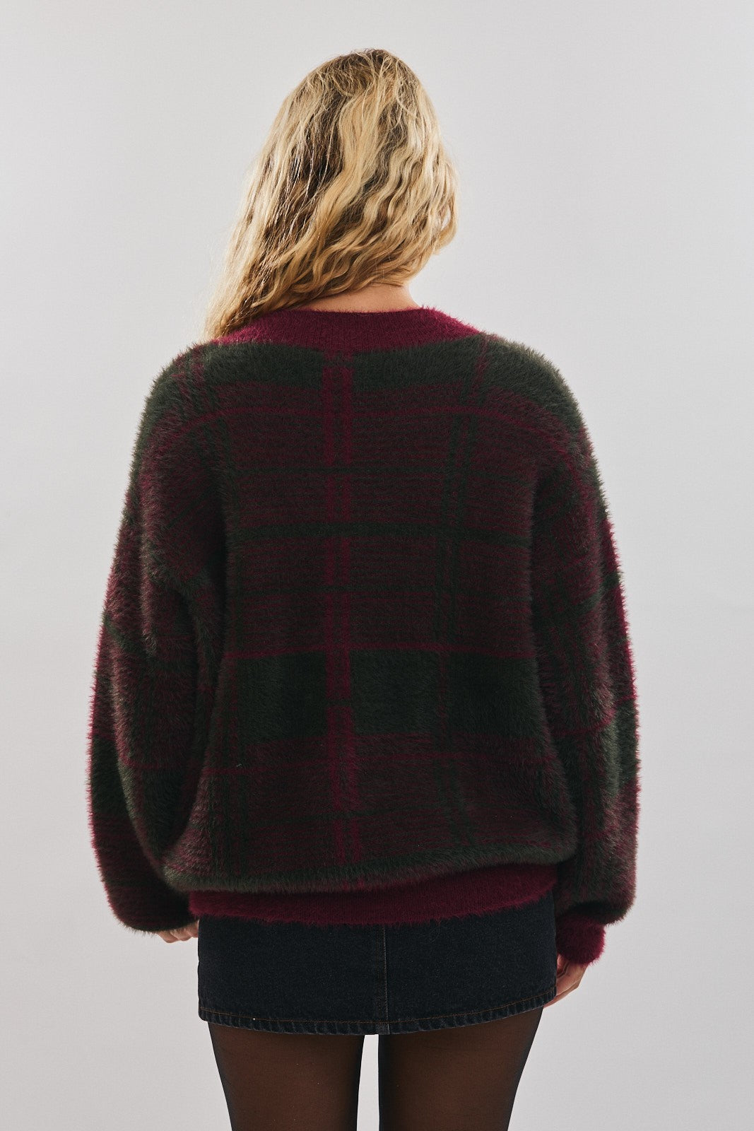Back view of a woman wearing a muted burgundy and green plaid sweater on a plain background