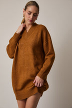 Woman wearing a camel sweater dress with black knee-high boots on a plain background