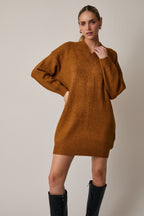Woman wearing a camel sweater dress with black knee-high boots on a plain background