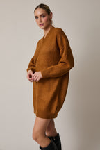 Woman wearing a camel sweater dress with black knee-high boots on a plain background