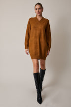 Woman wearing a camel sweater dress with black knee-high boots on a plain background