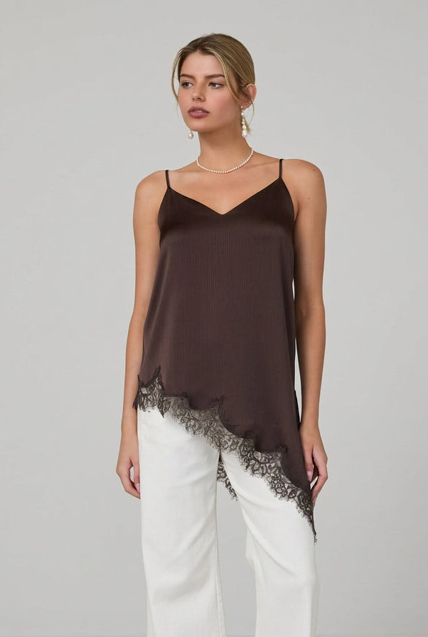 Woman wearing a brown satin asymmetrical lace hemmed cami tunic top and white pants in a minimalistic room.