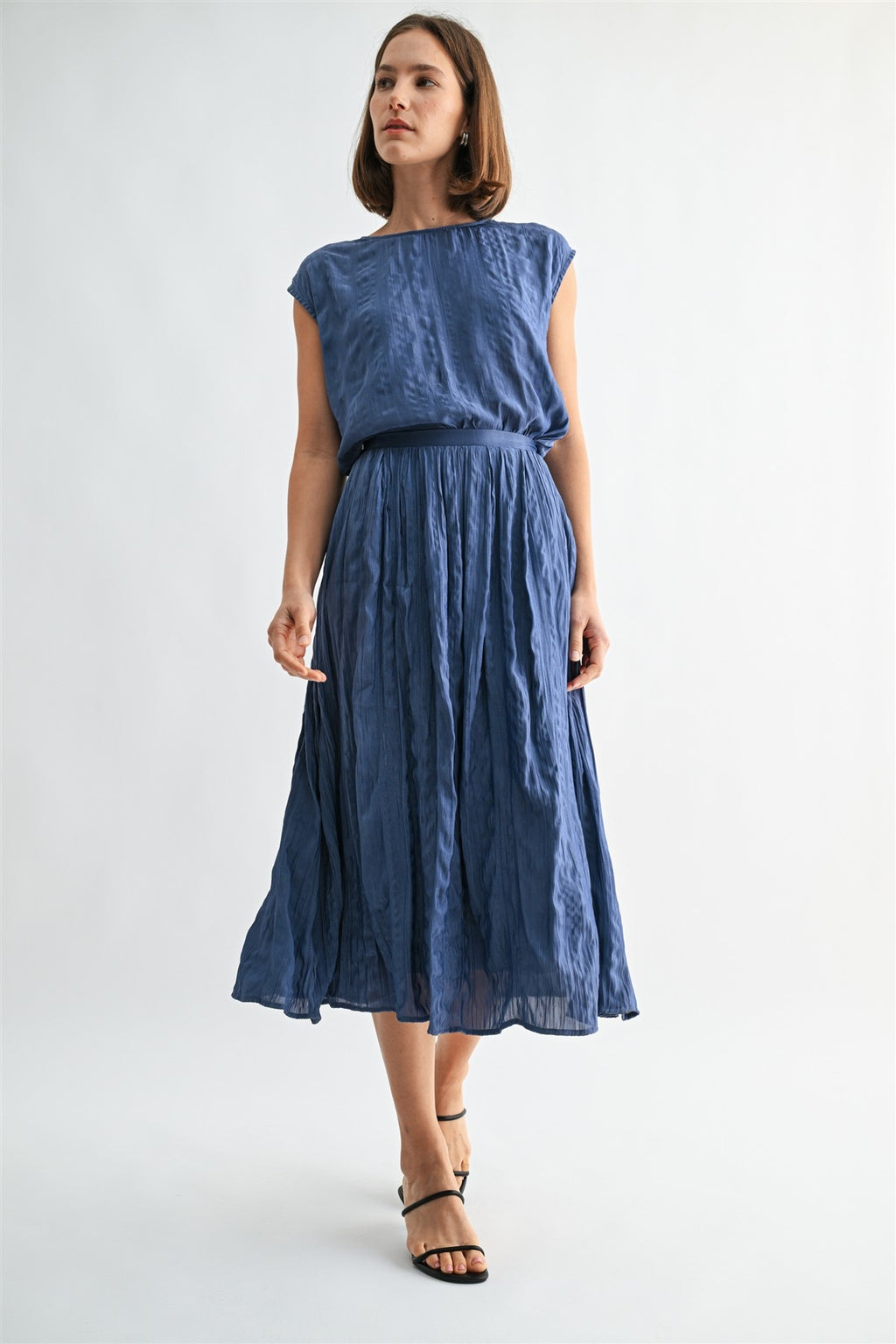 Woman wearing a dusty blue crinkle satin cap sleeve top and skirt against a light gray background