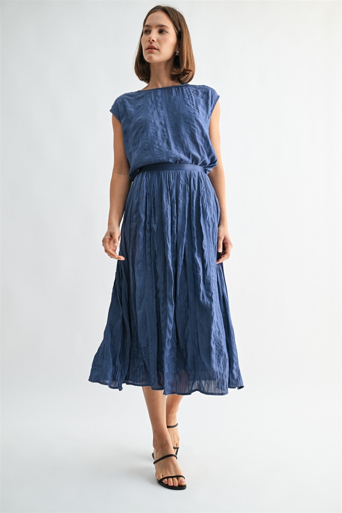 Woman wearing a dusty blue crinkle satin cap sleeve top and skirt against a light gray background