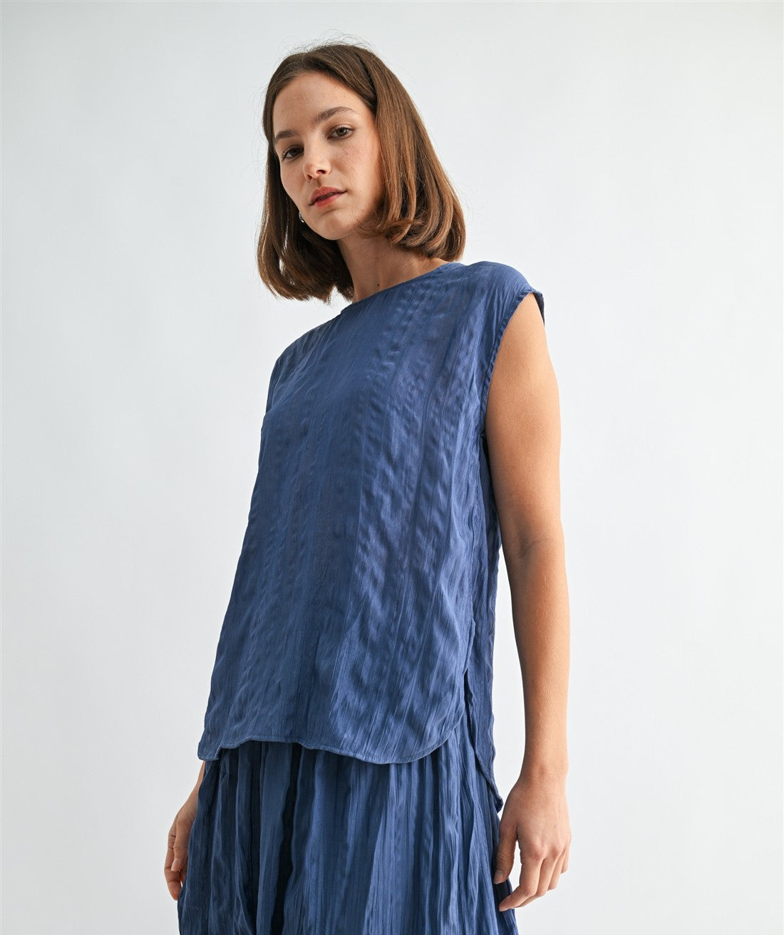 Woman wearing a dusty blue crinkle satin cap sleeve top against a light gray background