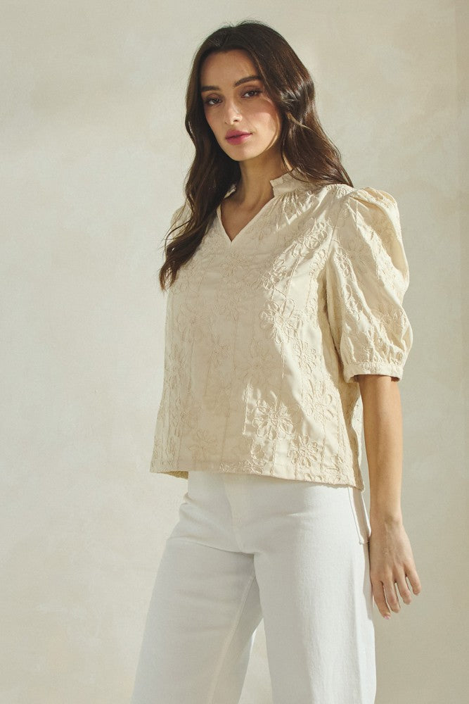 Woman wearing an ecru floral applique  blouse with puff sleeves against a plain background