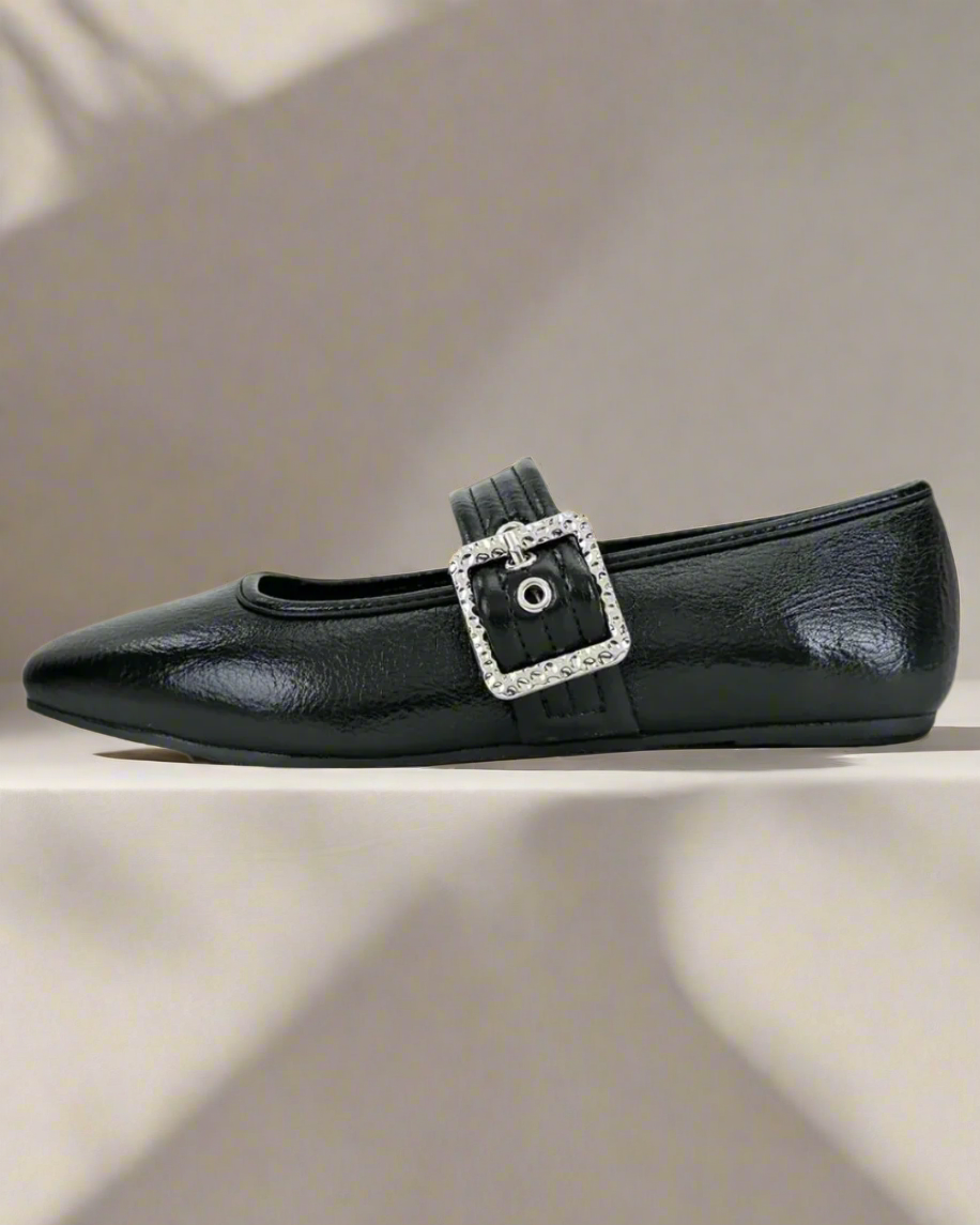 Black flat shoe with a decorative buckle on a neutral background