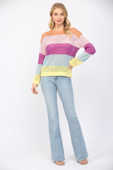 Woman wearing an open weave color block striped sweater and jeans on a white background