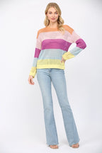 Woman wearing an open weave color block striped sweater and jeans on a white background