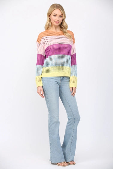 Woman wearing an open weave color block striped sweater and jeans on a white background