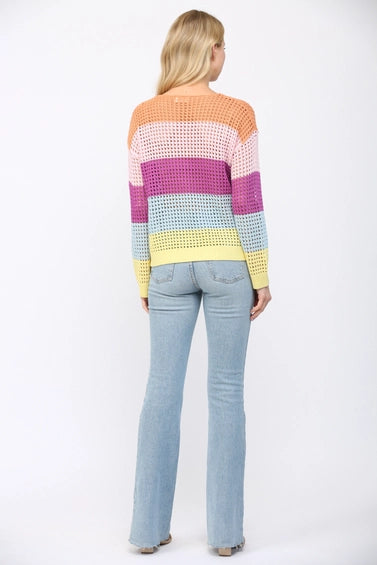 Back view of a woman wearing an open weave color block striped sweater and jeans on a white background